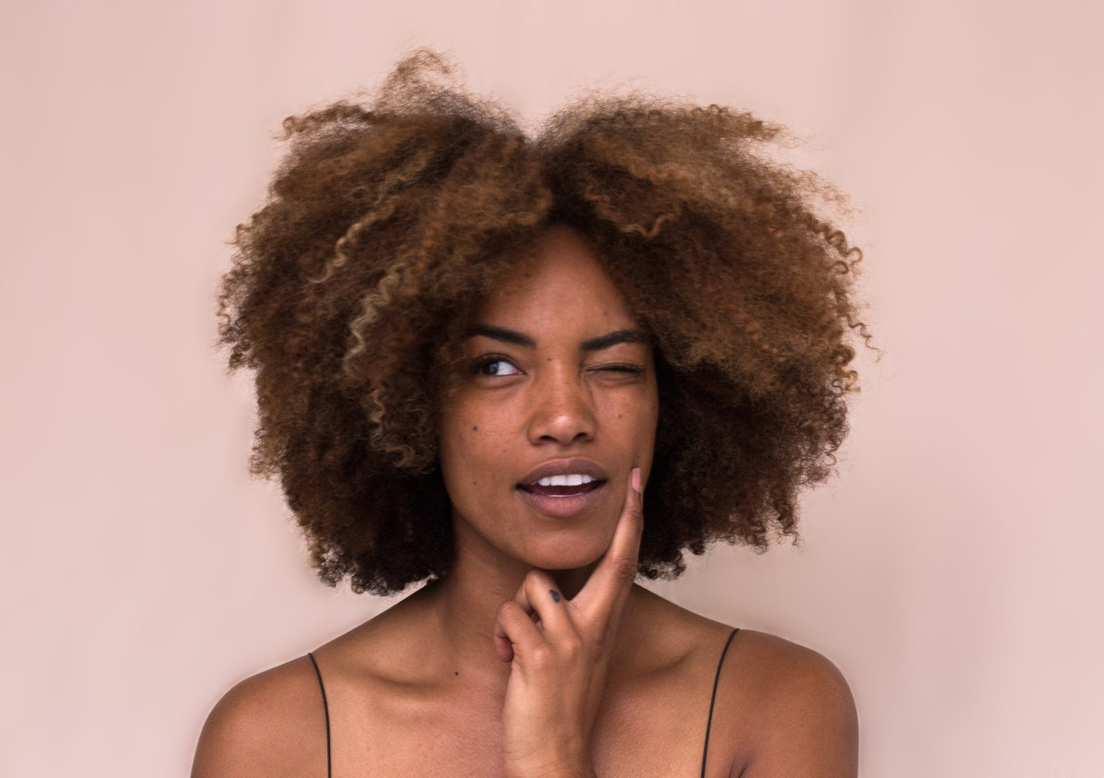 a black woman with gorgeous curly brown and blonde hair thinking